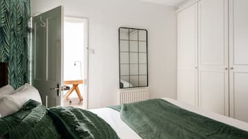 A bedroom with a bed, green pillows, a mirror, and a wardrobe.