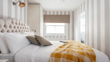 A bedroom with a tufted headboard, striped walls, a large window, and a checkered throw blanket.