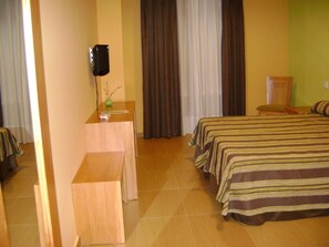 Habitación de hotel con dos camas, un escritorio con un altavoz y una silla.