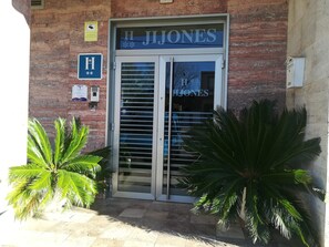 Entrada de un hotel con un cartel que dice "H. JONES" y un letrero azul con una 'H' blanca y estrellas.