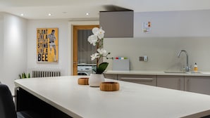 A modern kitchen with a central island, wooden bowls, a potted orchid, and a poster on the wall. - The Norfolk Townhouse - Large & Stunning 5BDR Mews Home on Private Street (London)