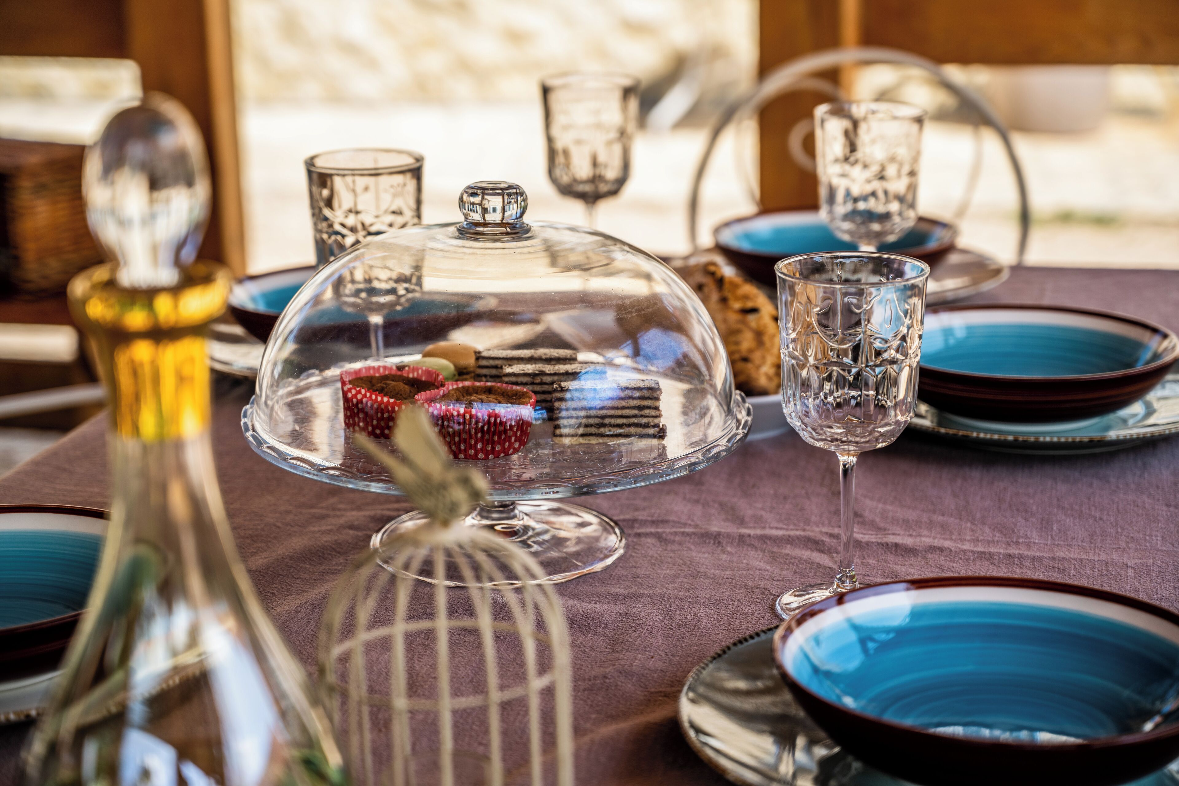 A table set with blue plates, clear glassware, and a glass dome cover.
