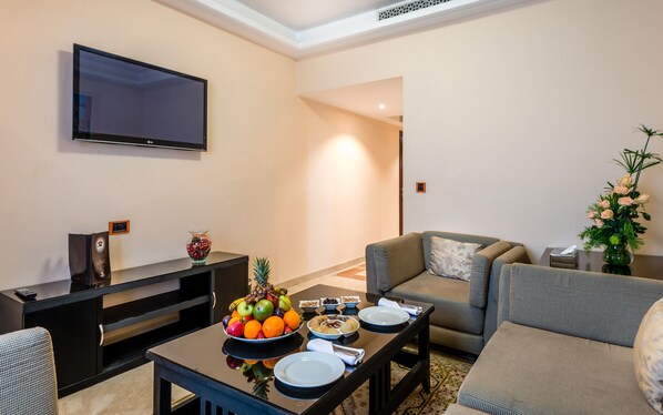 Una sala de estar moderna con un televisor de pantalla plana, una mesa de centro con fruta y aperitivos, un sofá y una mesita auxiliar.