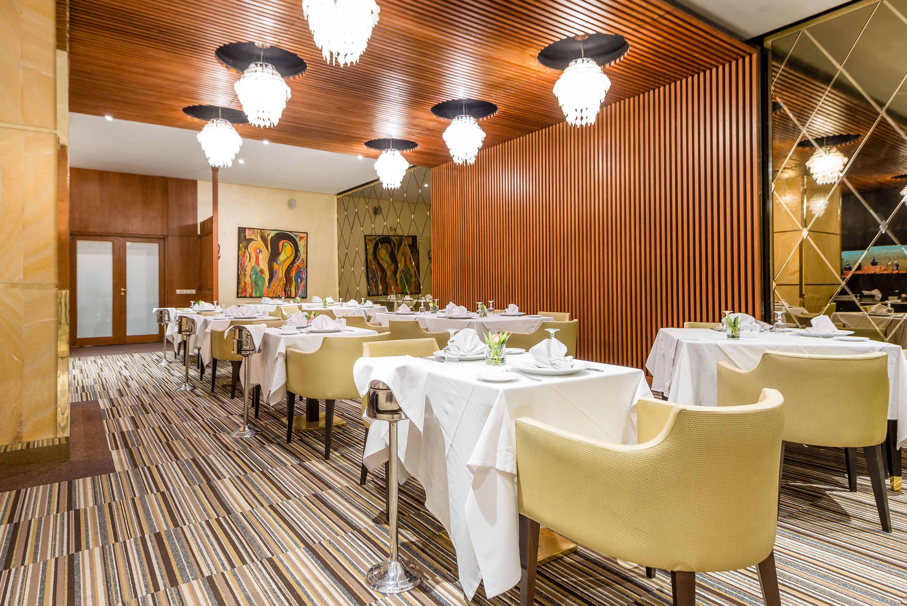 A dining area with multiple tables set for guests, featuring a patterned carpet and wooden paneling on the walls.