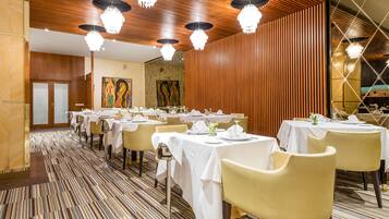A dining area with multiple tables set for guests, featuring a patterned carpet and wooden paneling on the walls.