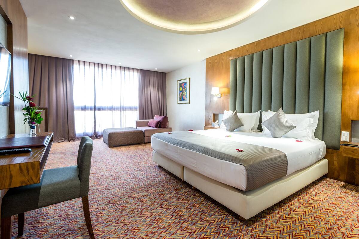 A hotel room with a large bed, a desk, a chair, and a sofa.