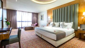 A hotel room with a large bed, a desk, a chair, and a sofa.