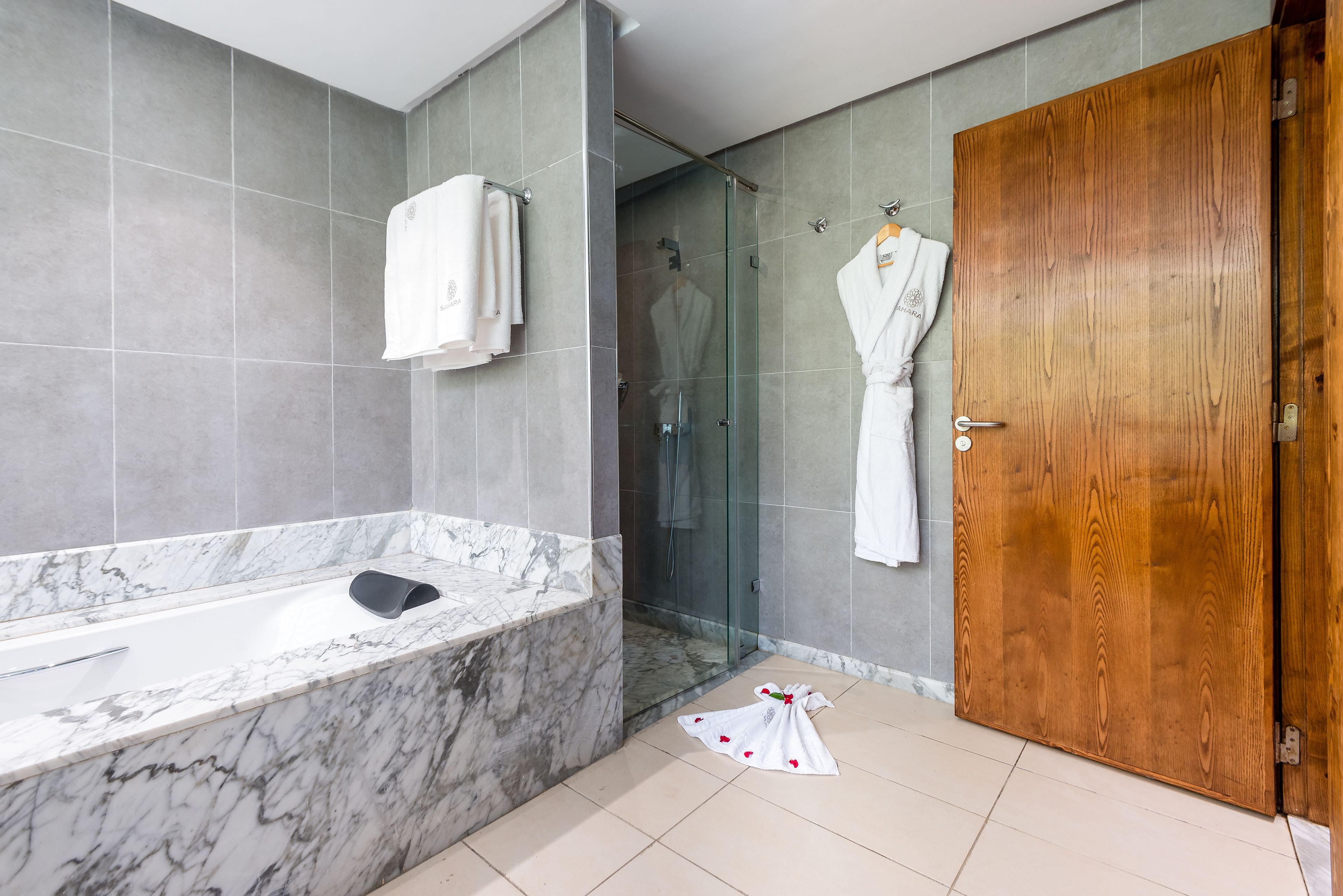 A modern bathroom with a marble bathtub, glass shower enclosure, and wooden door.