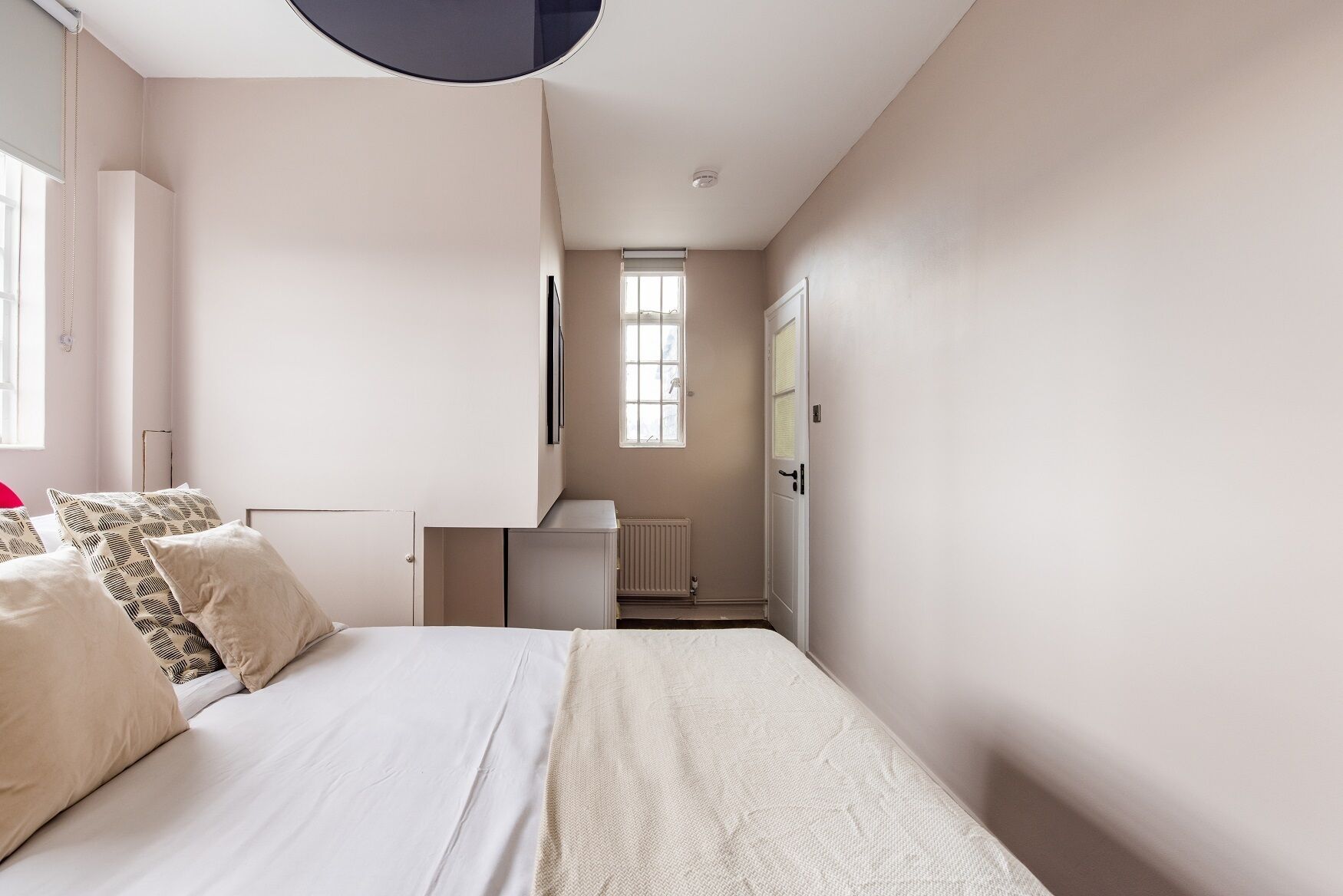 A bedroom with a bed, a radiator, a window, and a door.