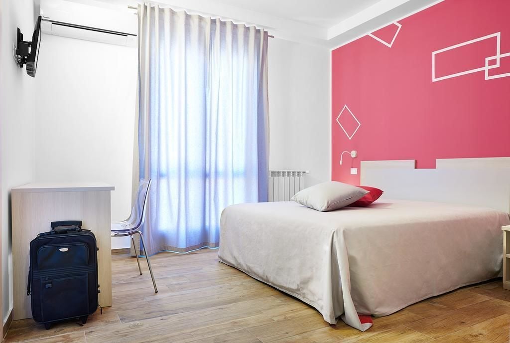 A hotel room with a bed, a desk, a chair, and a suitcase.