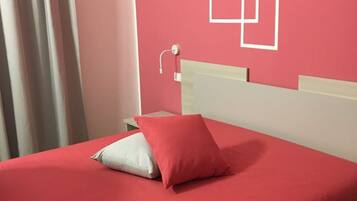 Un lit avec une couvre-lit rouge et deux oreillers, une tête de lit blanche et un mur orné de motifs géométriques blancs.