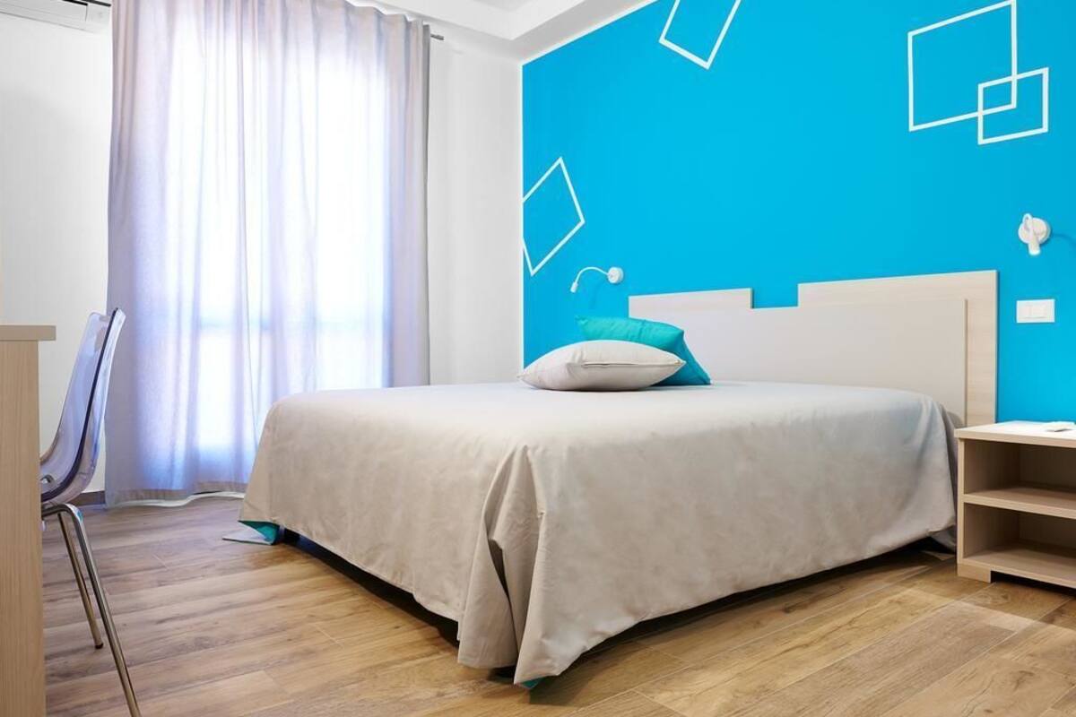 A bedroom with a bed, a nightstand, a chair, and a window with curtains.