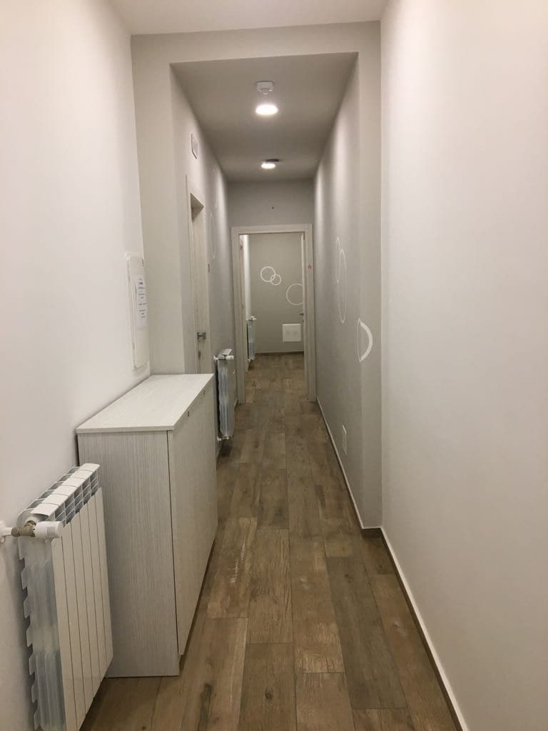 Corredor estreito com um radiador à esquerda, uma porta no final e um acessório de iluminação no teto.