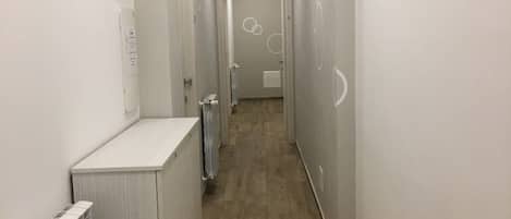 A narrow hallway with a radiator on the left, a door at the end, and a light fixture on the ceiling.