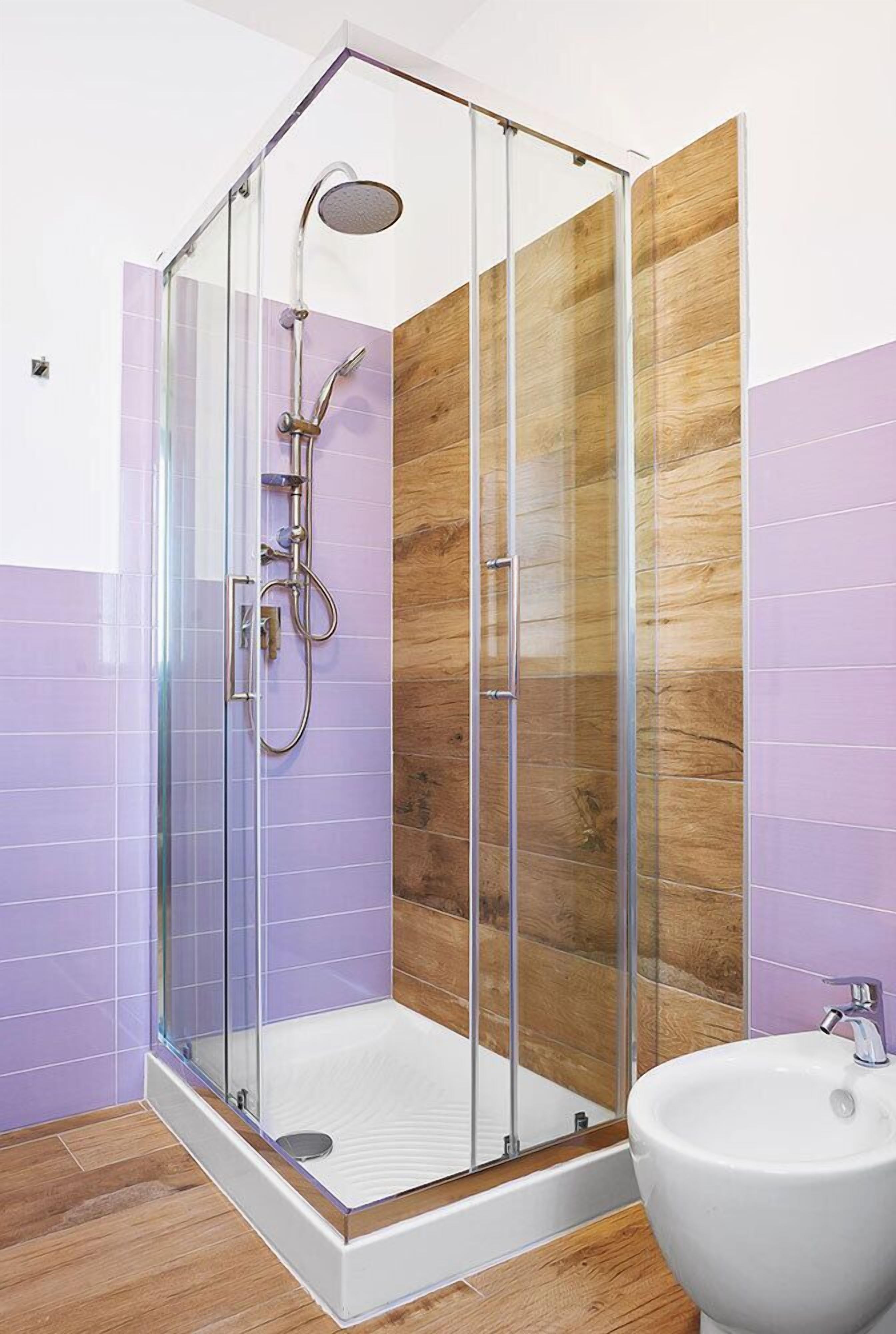 Un baño moderno con ducha envuelta en vidrio, paneles de madera y un lavamanos blanco.