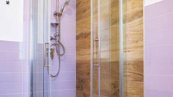Un baño moderno con ducha envuelta en vidrio, paneles de madera y un lavamanos blanco.