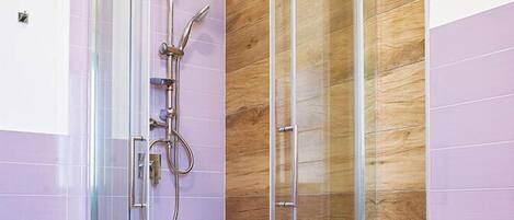 Un baño moderno con ducha envuelta en vidrio, paneles de madera y un lavamanos blanco.