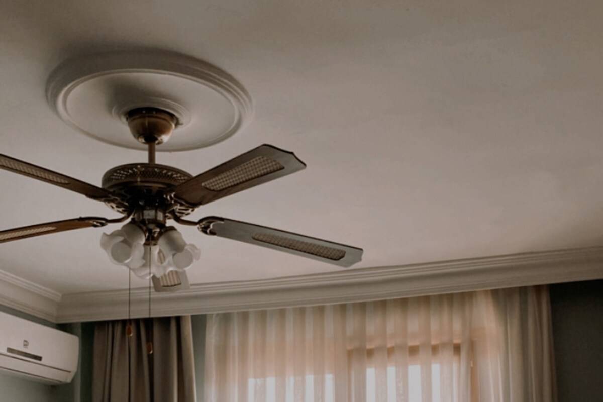 A hotel room with a ceiling fan, two chairs, a small table, and a bed.