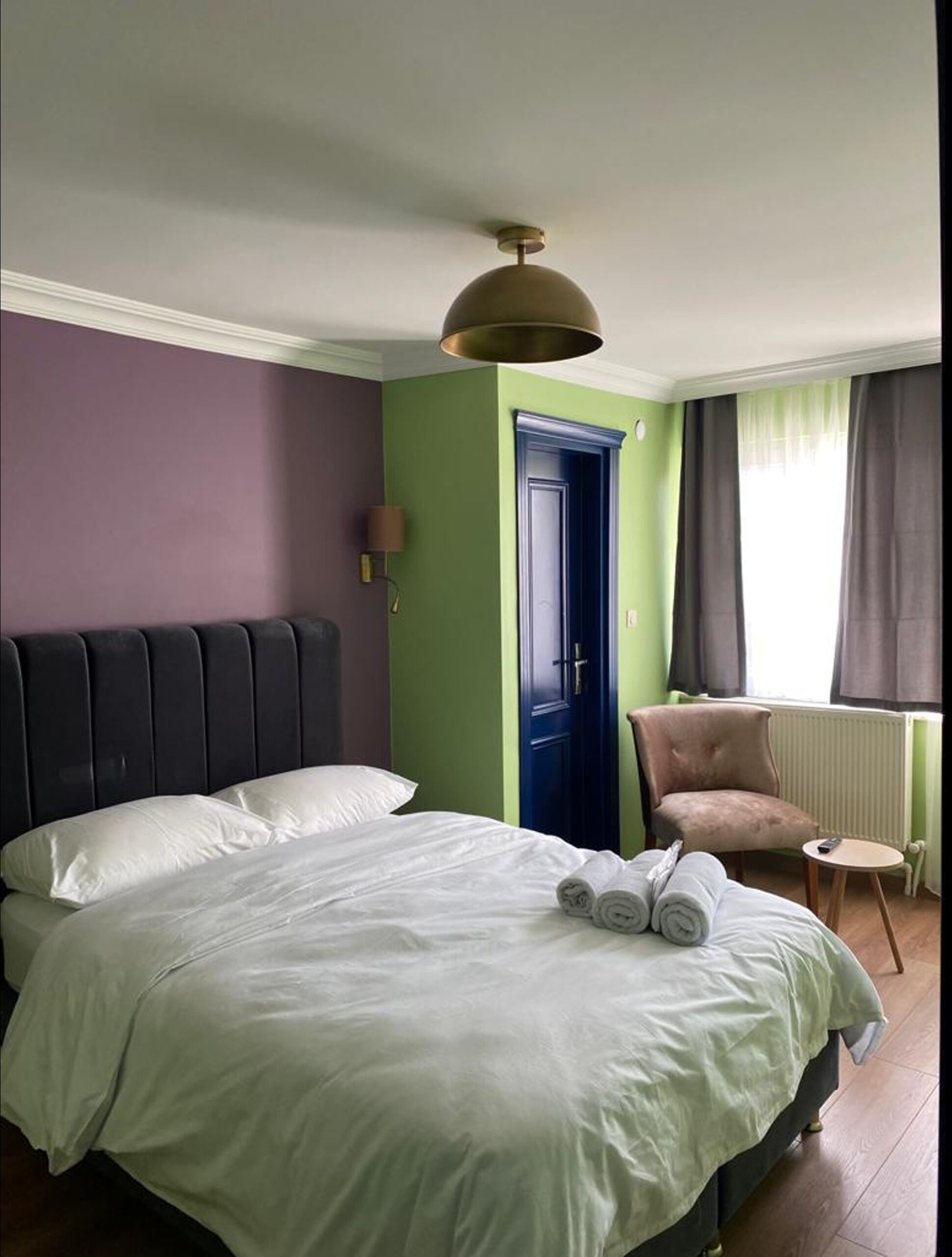 A hotel room with a bed, a chair, a door, and a window with curtains.