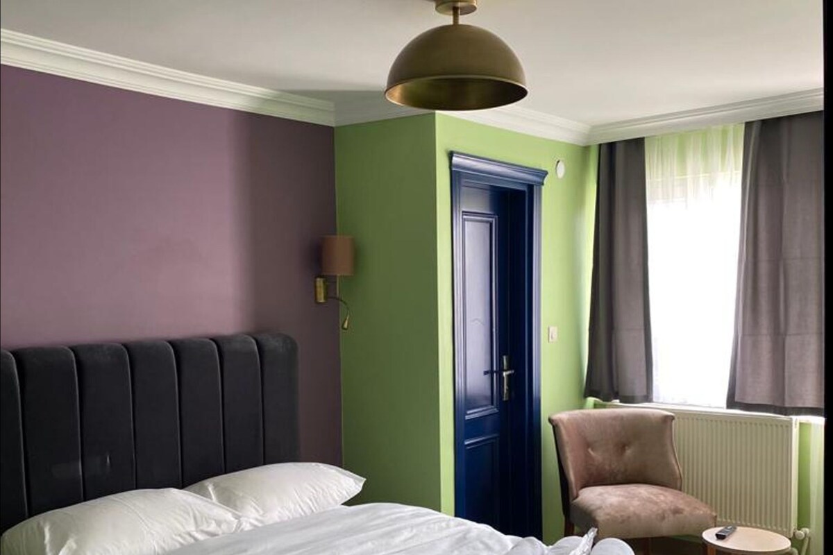A hotel room with a bed, a chair, a door, and a window with curtains.