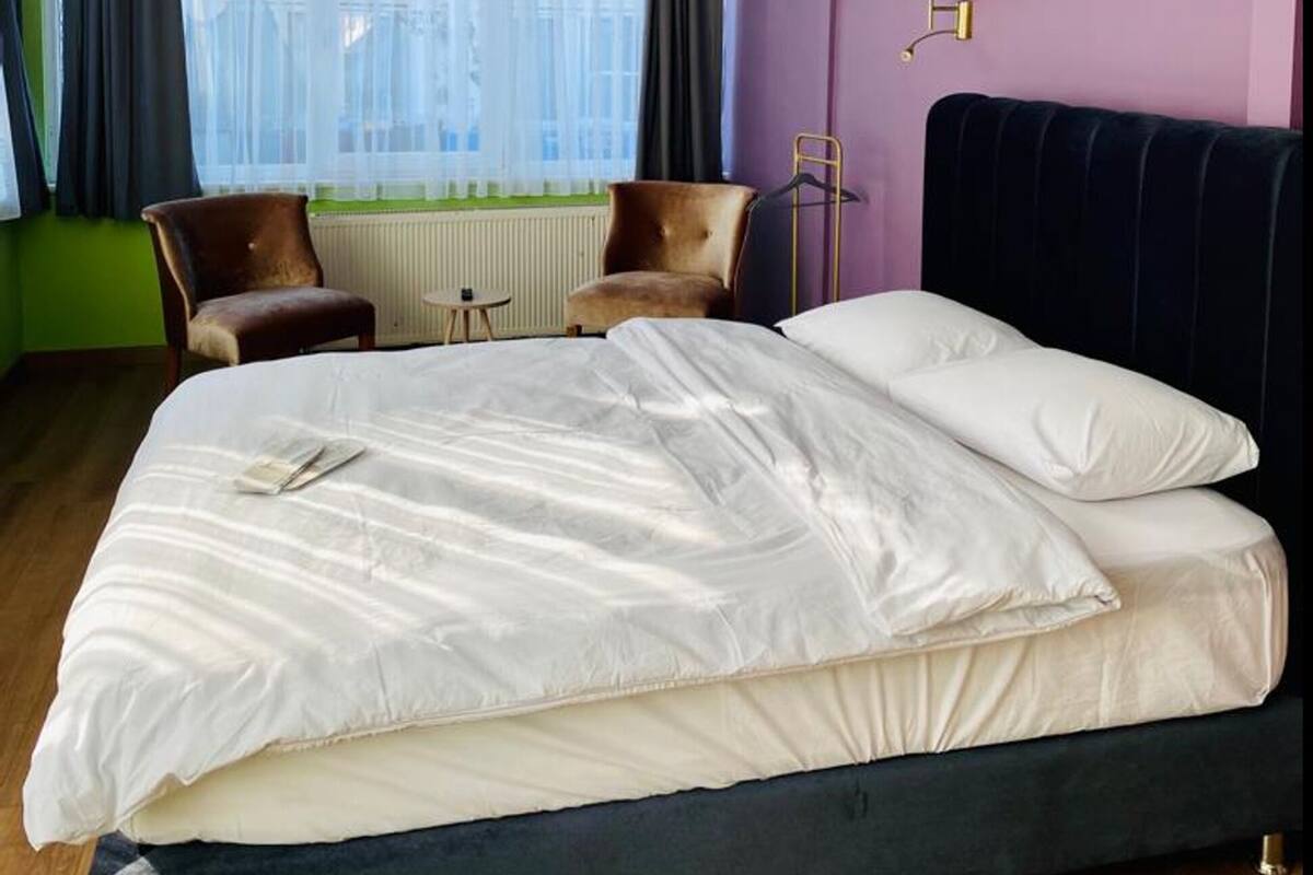 Une chambre d’hôtel avec un lit, une chaise, un radiateur et une fenêtre avec des rideaux.