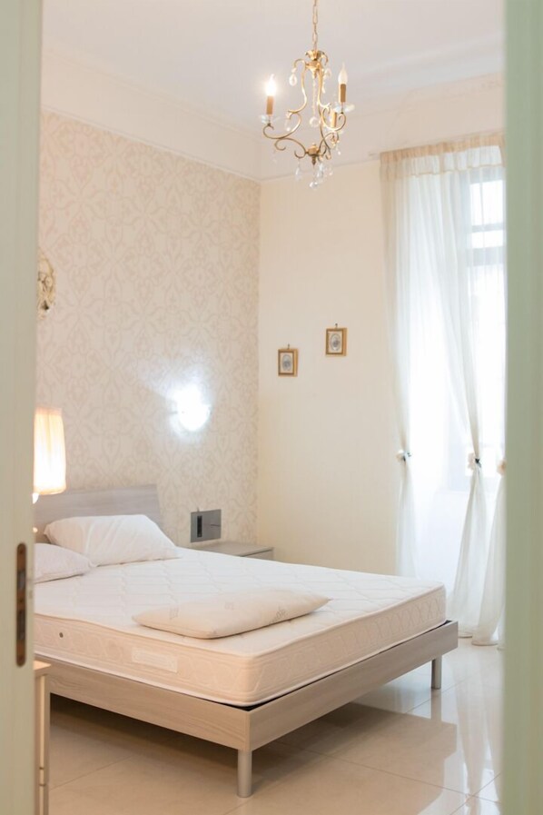Een slaapkamer met een bed, nachtkastje, een wandlamp en een kroonluchter.