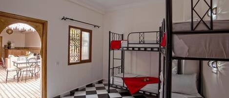 A room with a checkered floor, bunk beds, a dining area with chairs and a table, and a window with decorative glass.