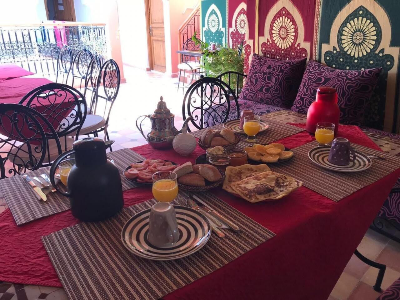 Mesa de café da manhã posta com diversos pratos, incluindo pão, doces e uma jarra de suco de laranja.