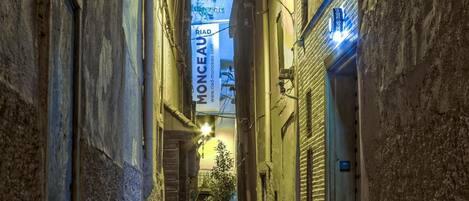 A narrow alleyway with a hostel sign, a door with a blue sign, and a street lamp.