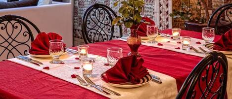 A dining table set with red tablecloths, candles, and rose petals.