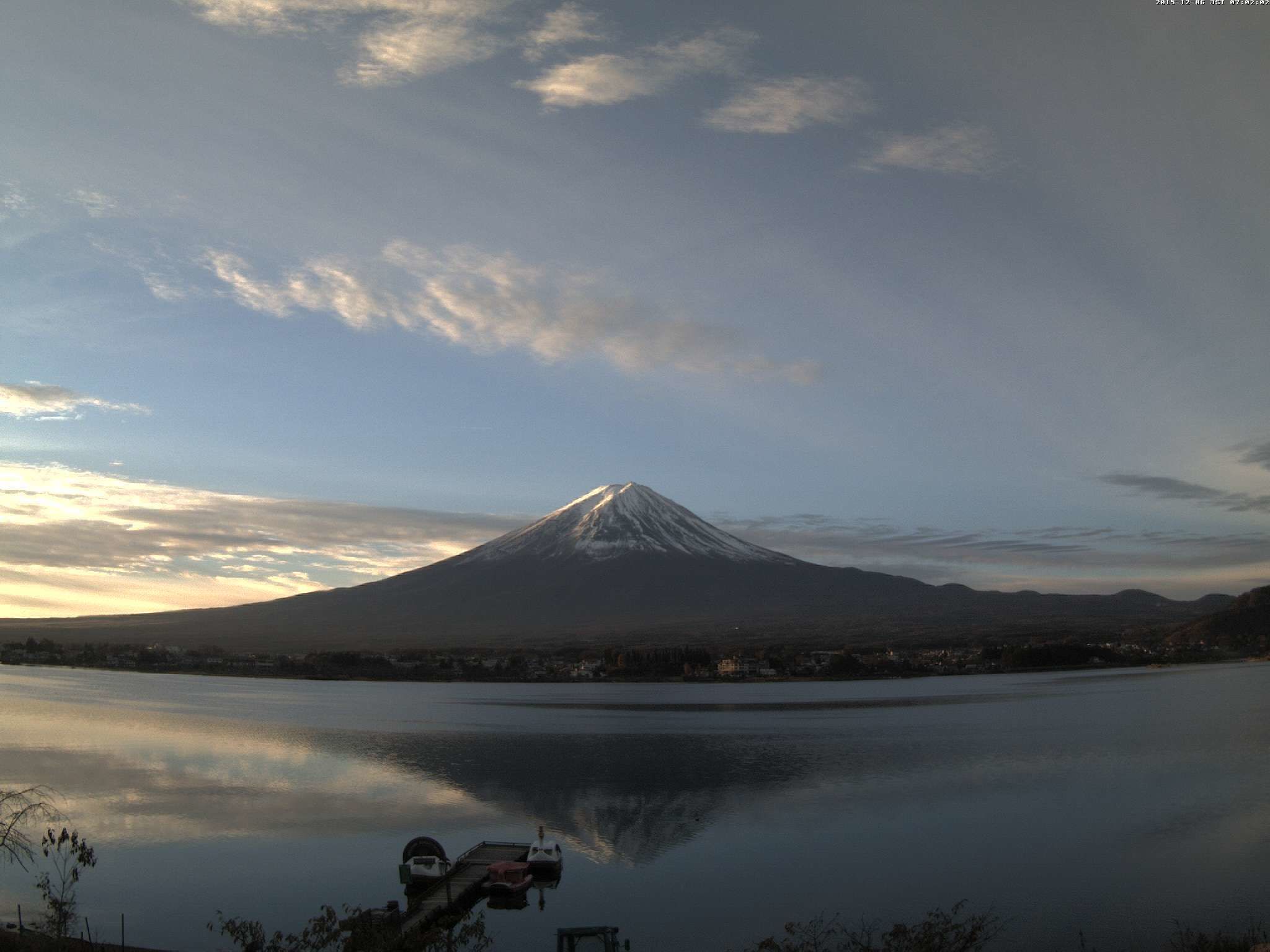 Una montaña con un lago al frente y un muelle con barcos.