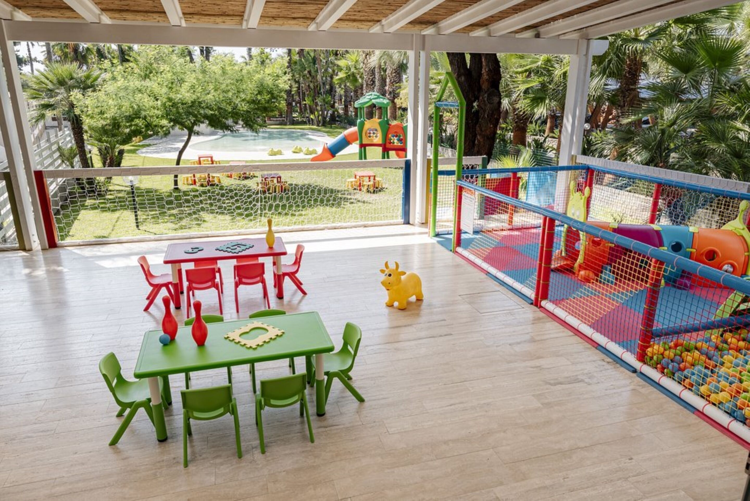 Ein Spielbereich für Kinder mit Rutsche, Netzspielelementen und einem Tisch mit Stühlen.