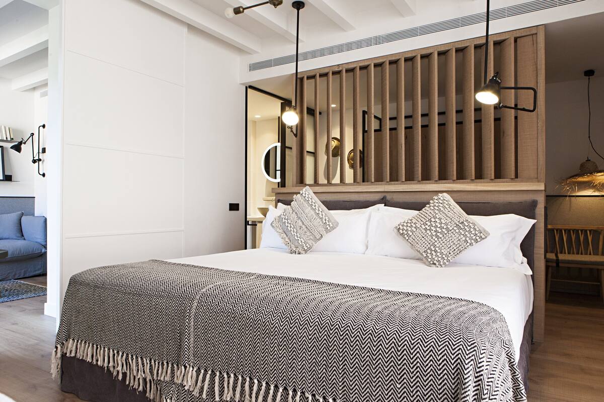 Une chambre moderne avec un grand lit, une tête de lit en bois et des luminaires suspendus.