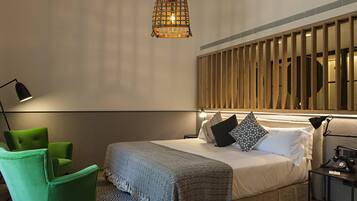 A modern bedroom with a large bed, a green armchair, a bedside table with a lamp, and a hanging light fixture.