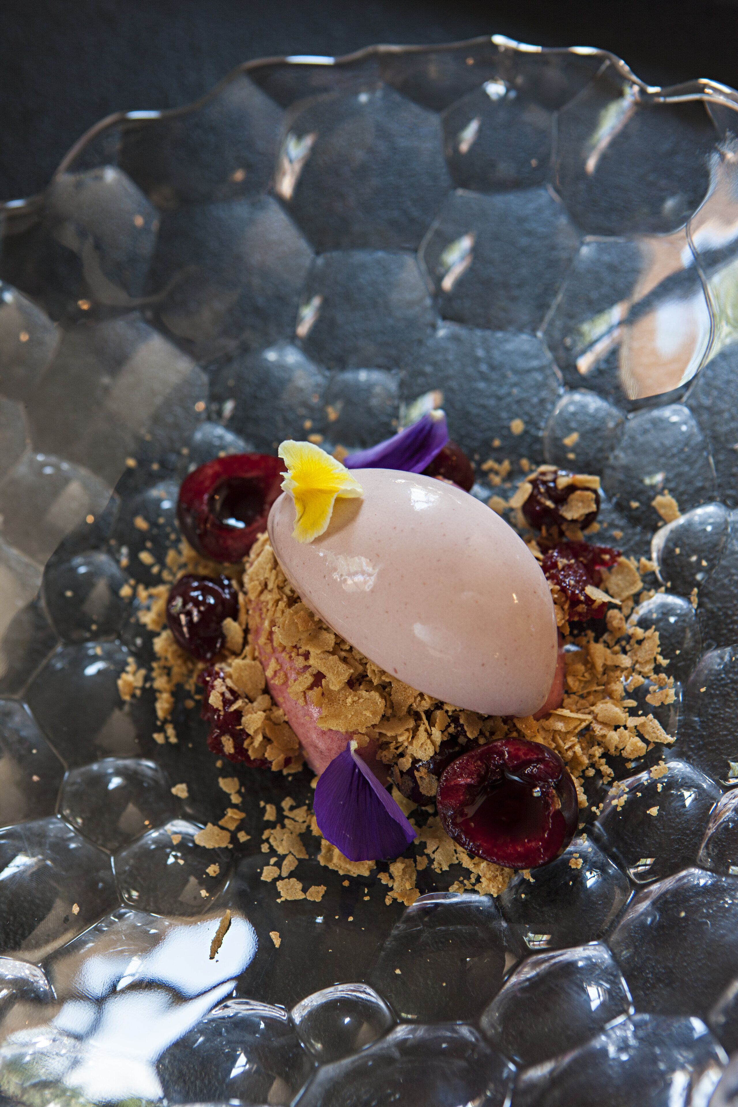Un postre sobre un plato de vidrio con bayas y una flor.
