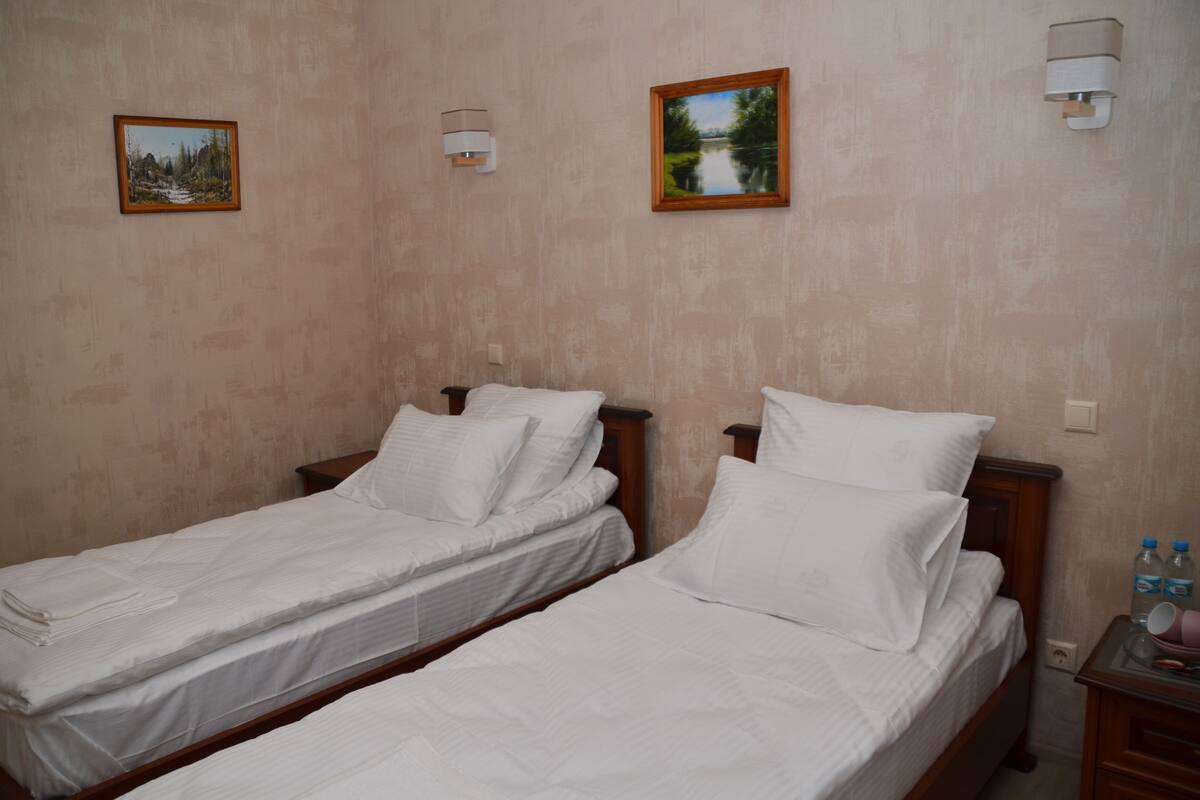 Two single beds with white linens, wooden headboards, and a nightstand with a water bottle and a cup.