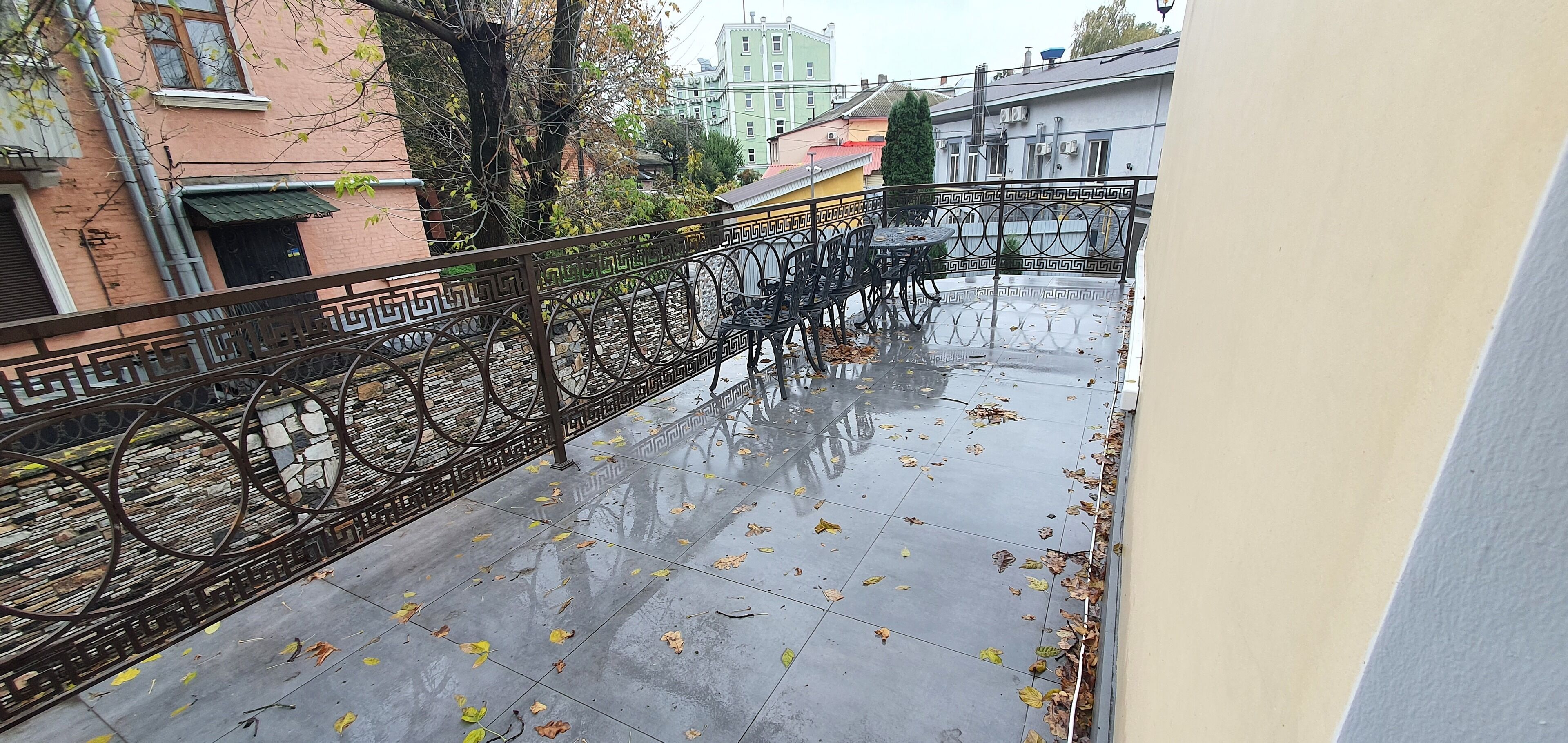 Un balcón con barandilla metálica, piso de baldosas y hojas otoñales dispersas.