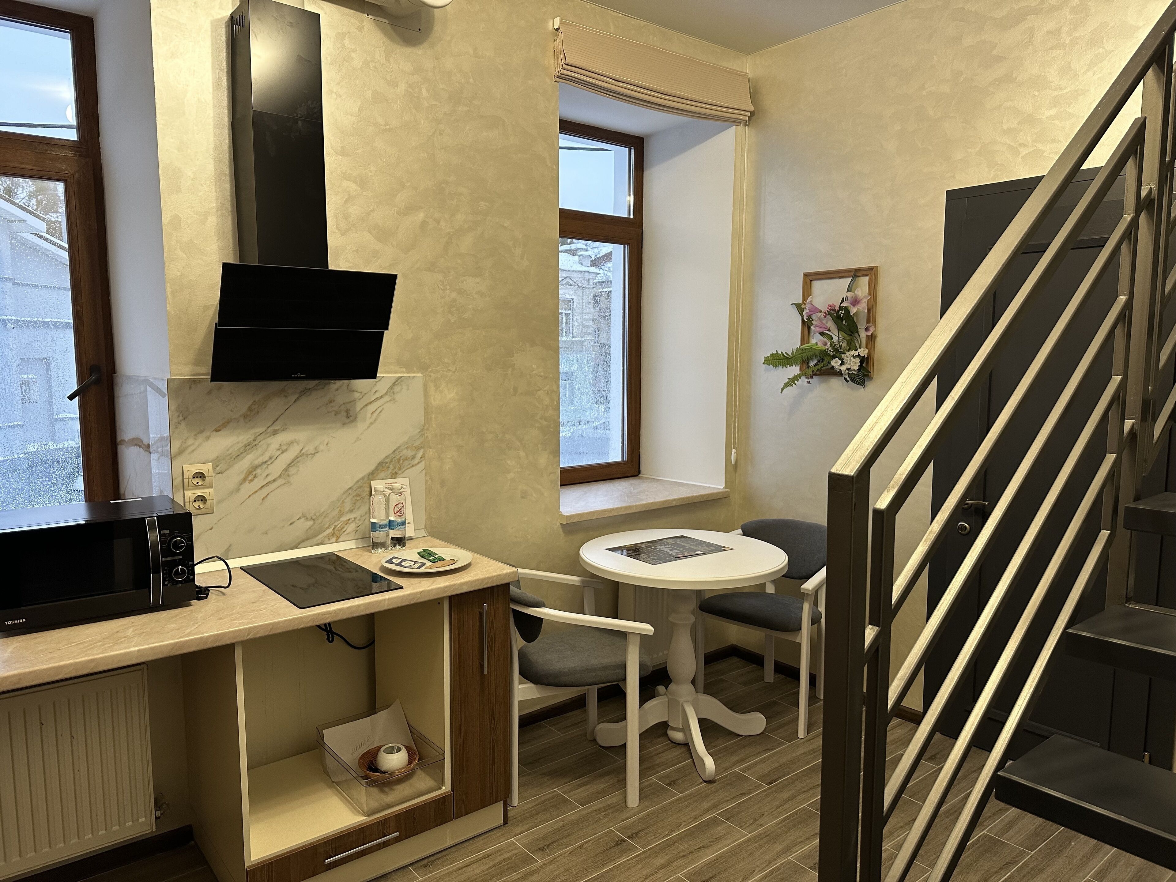 A compact hotel room with a kitchenette, a flat-screen TV, a small dining table, and a staircase.