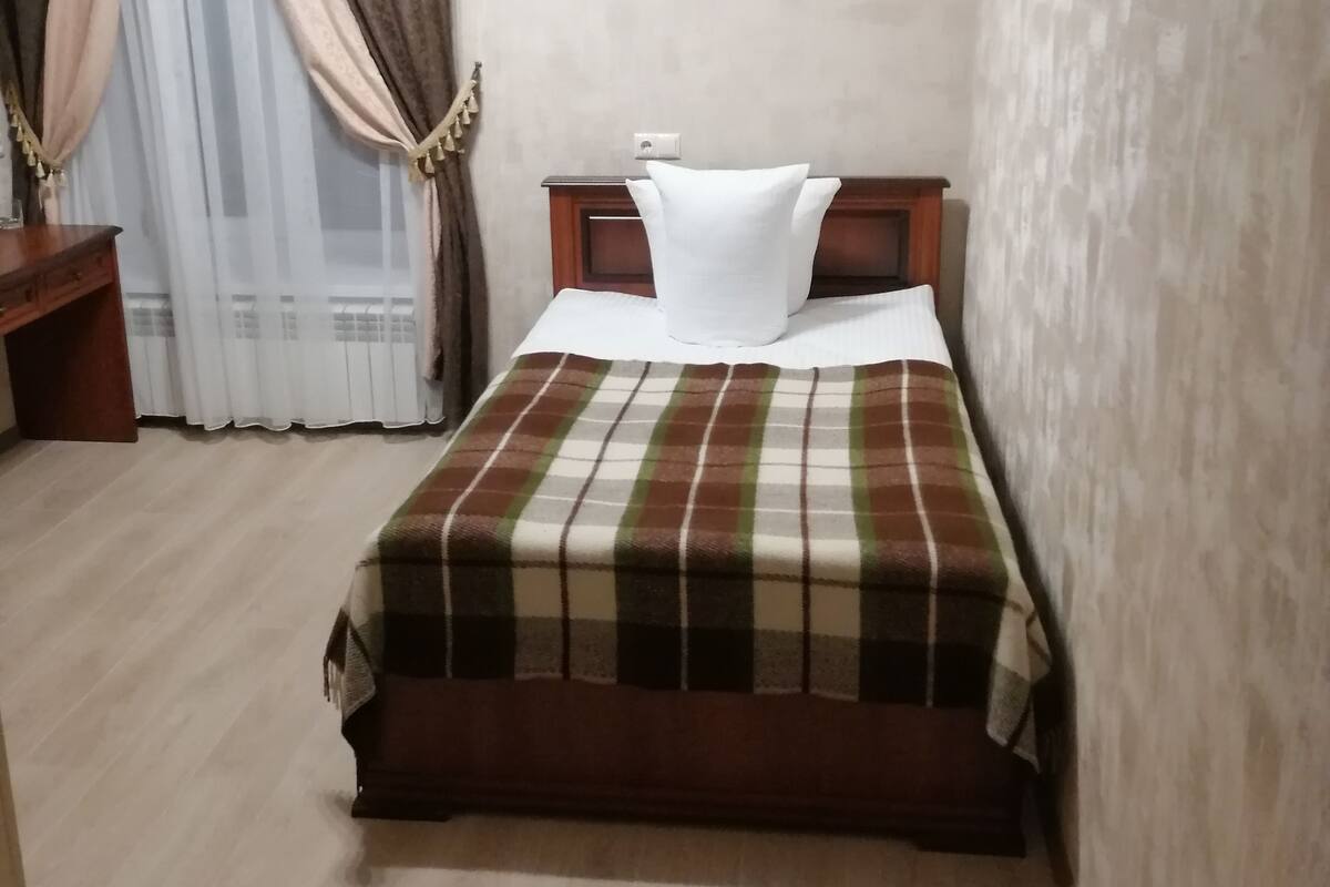 A bedroom with a bed, a nightstand, a lamp, and a window with curtains.