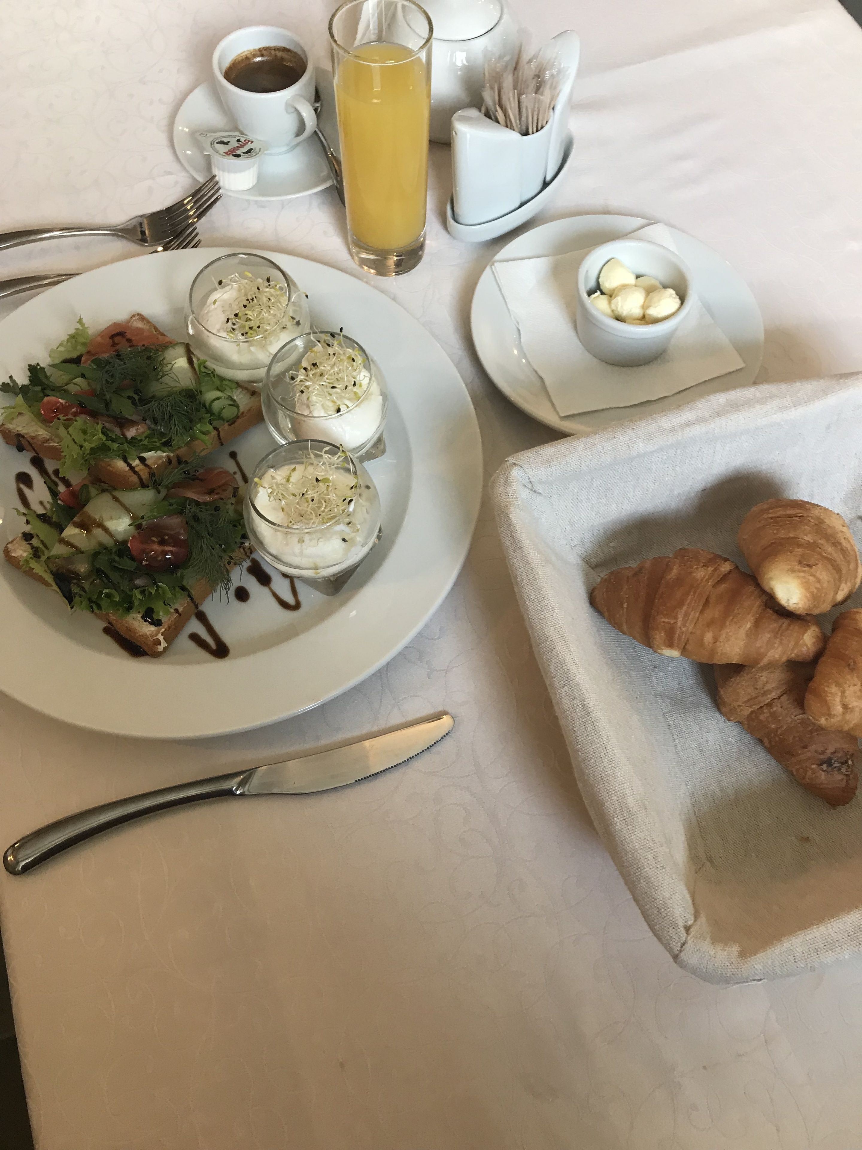 En frukostuppläggning med croissanter, en tallrik med sallad och ett glas apelsinjuice.