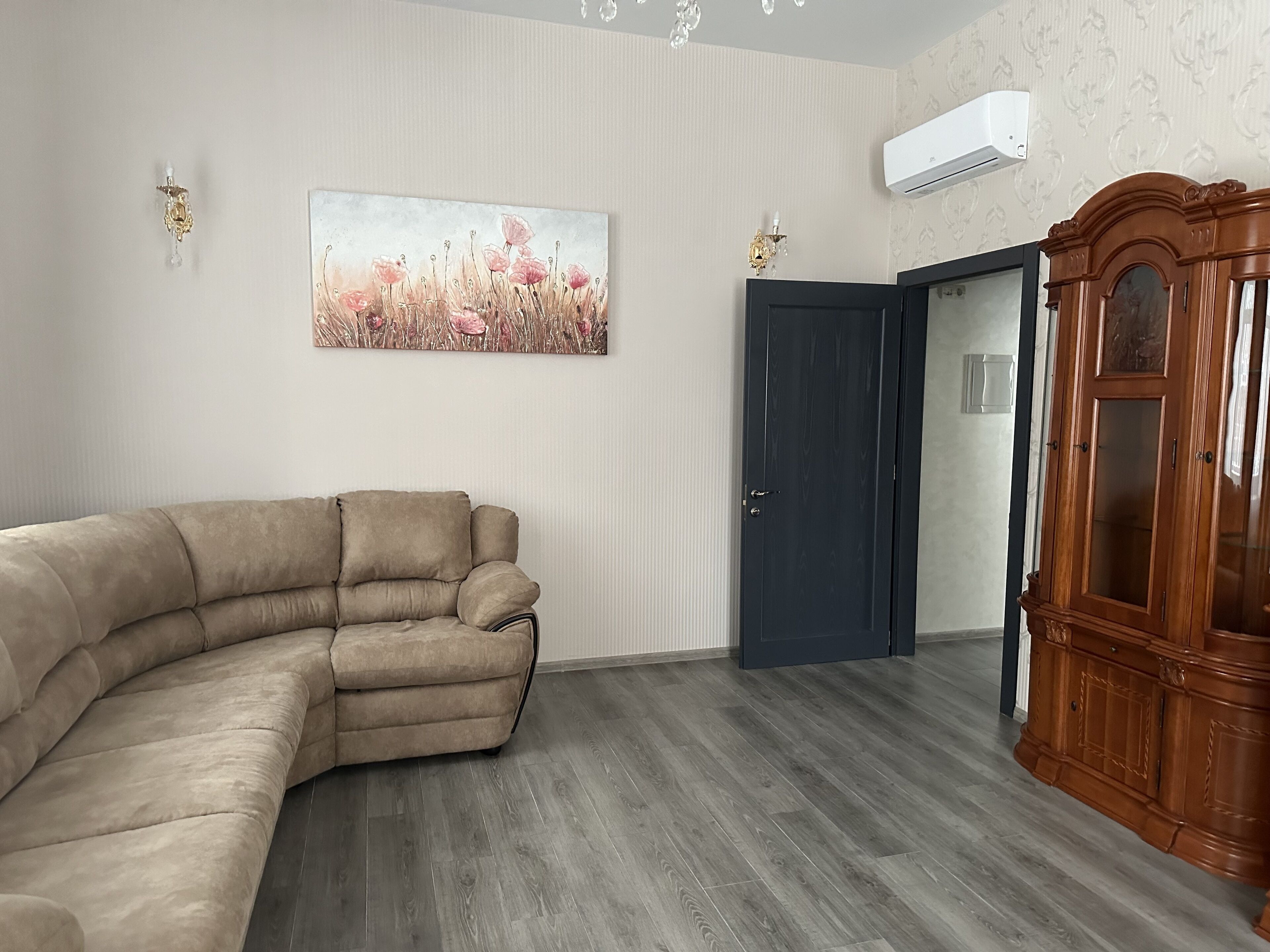 A living room with a beige sectional sofa, a dark wooden door, and a wooden cabinet.