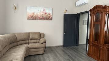 A living room with a beige sectional sofa, a dark wooden door, and a wooden cabinet.