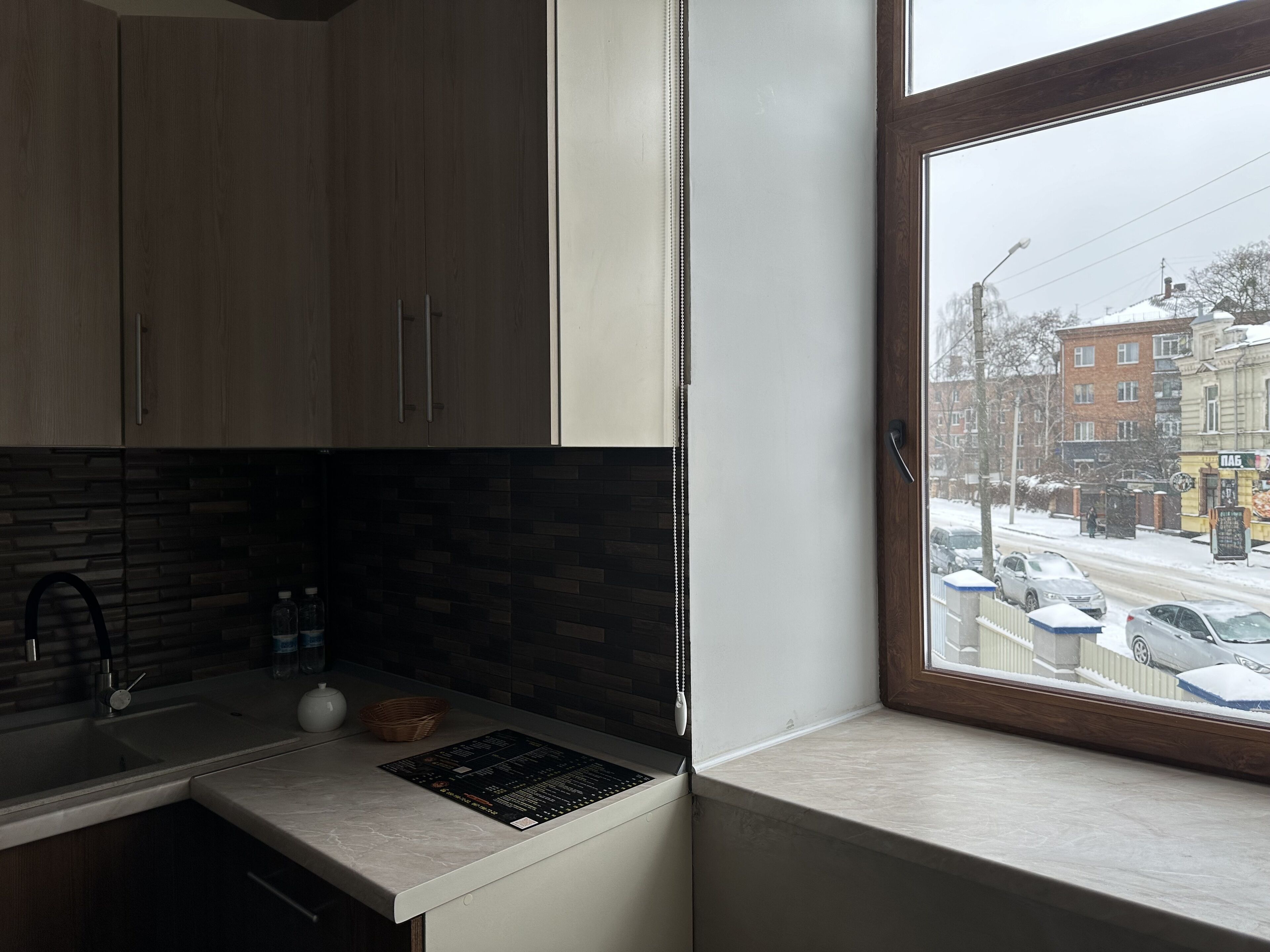 Eine Küche mit Holzschränken, einer gefliesten Spritzschutzwand und einem Fenster mit Blick auf eine verschneite Straße.
