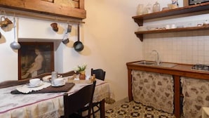 A compact kitchen with a wooden countertop, hanging pots, a sink, and a dining area with a table set for two. - Novecento B&B (Massafra)