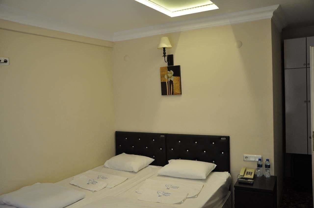 A hotel room with a bed, a nightstand with a lamp, a painting on the wall, and a wardrobe.