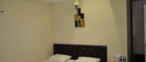 A hotel room with a bed, a nightstand with a lamp, a painting on the wall, and a wardrobe.