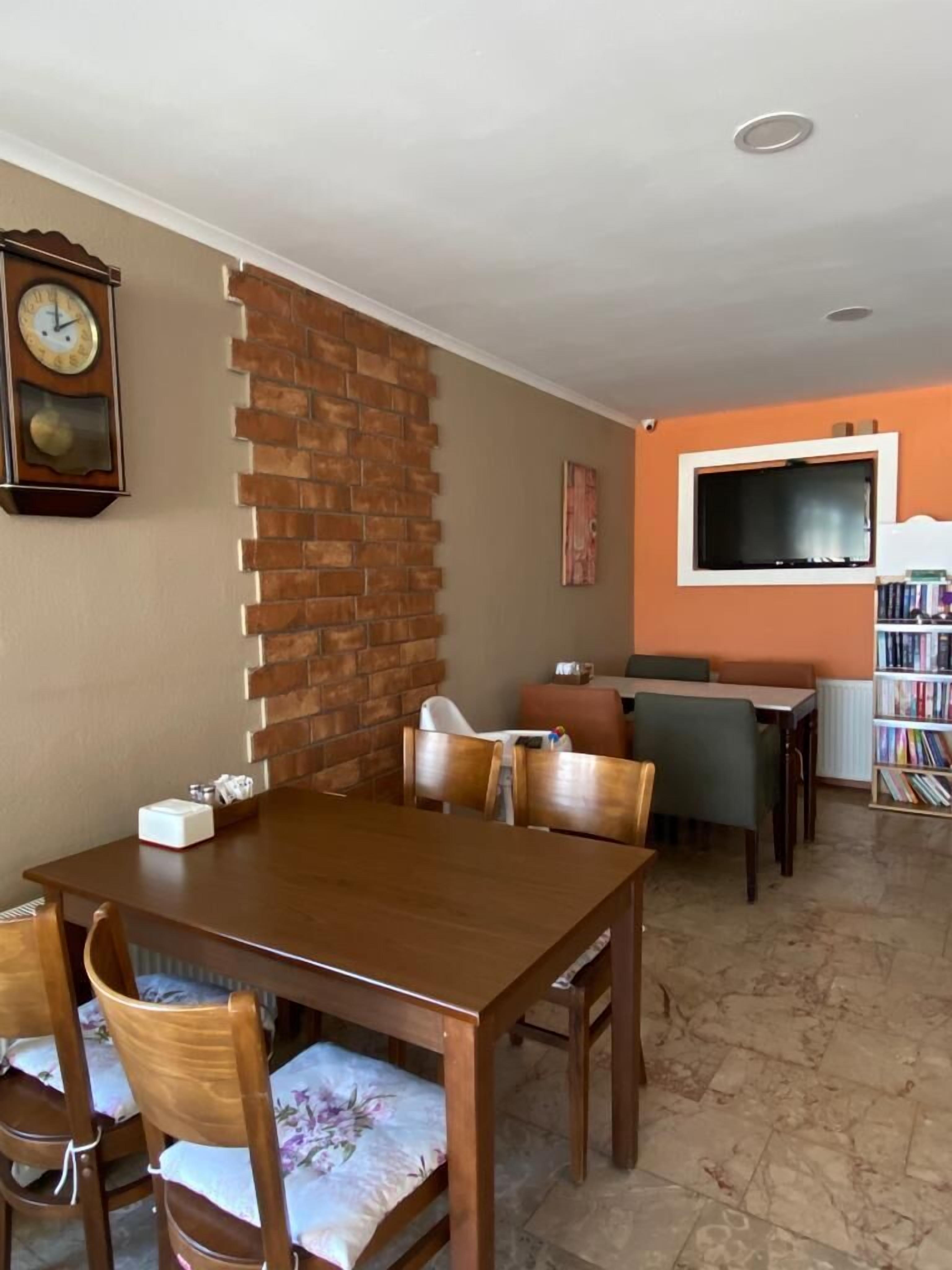 Ein Essbereich mit einer Wand aus Ziegelsteinen, einem Holztisch und Stühlen. An der Wand hängt eine Uhr und ein Bücherregal ist mit Büchern gefüllt.
