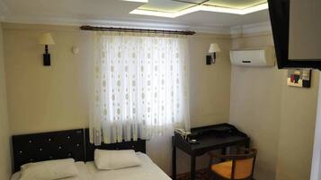 A hotel room with a bed, a desk, and an air conditioning unit.