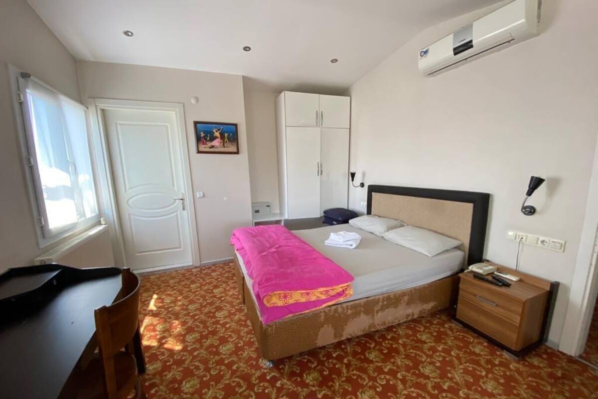 A bedroom with a bed, a desk, a wardrobe, and an air conditioning unit.