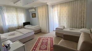 A hotel room with two single beds, a sofa, a small table, and a red patterned rug. - Şakran Otel (Aliaga)